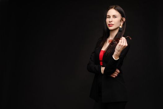 Portrait of young beautiful woman thoughtfully looking down. Brunette model in elegant costume posing at camera . Pretty lady in red sunglasses leaning one hand on other and holding it near face.