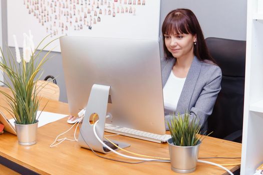 A brunette woman at a computer in the workplace. Business concept.
