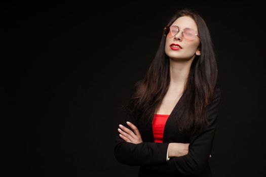 Portrait of young beautiful woman thoughtfully looking down. Brunette model in elegant costume posing at camera . Pretty lady in red sunglasses leaning one hand on other and holding it near face.