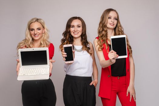 Three gorgeous elegant young women in casual clothes using laptop, mobile phone and tablet. They are using gadgets for work and communication.