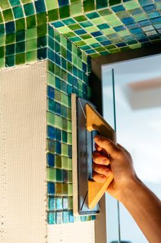 Worker applying mosaic tiles in bathroom walls. Bath renovation.
