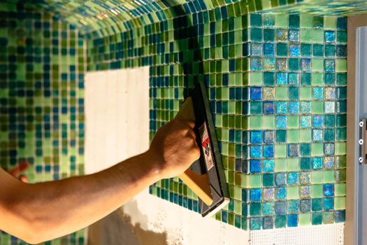 Worker applying mosaic tiles in bathroom walls. Spa or sauna relaxation modern room interior design.