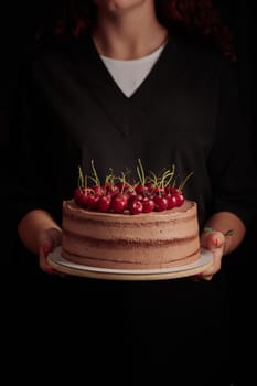 Cake with berries in woman's hands on a black background