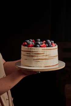 Cake with berries in woman's hands on a black background