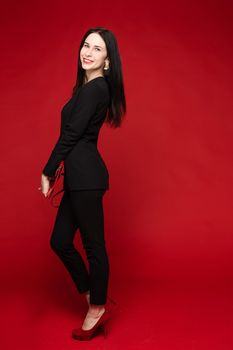 Portrait of young beautiful woman thoughtfully looking down. Brunette model in elegant costume posing at camera . Pretty lady in red sunglasses leaning one hand on other and holding it near face.