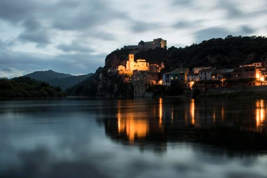 Miravet enlightened and beautiful town and its reflection on the river in Catalonia in a long exposure picture