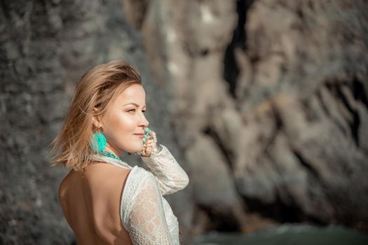 Middle aged woman looks good with blond hair, boho style in white long dress on the beach decorations on her neck and arms