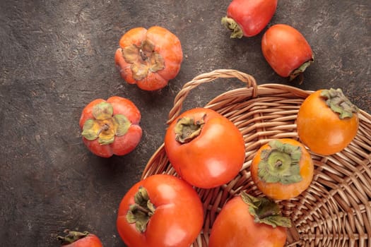 Different fresh persimmons on a dark background