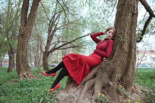 a girl in red rests leaning on a tree in the spring forest