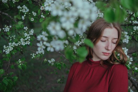 a blonde girl in red unites with nature in a garden of flowering trees