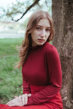 a girl in red sits under a tree in the spring forest and enjoys nature