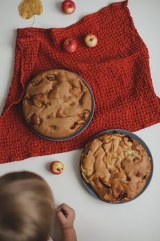 Baby hands reach for the apple cake on white table top view.