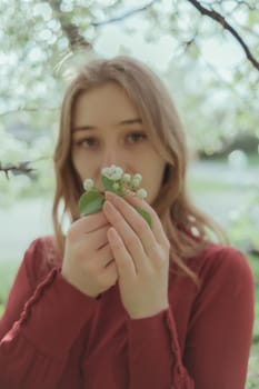 a blonde girl in red inhales the smell of cherry blossoms