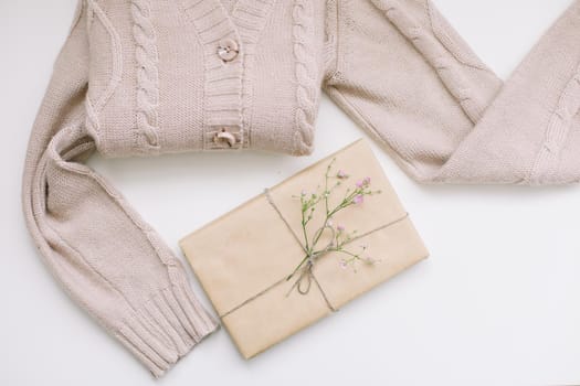beige knitted sweater and a gift in craft paper, top view, copy space