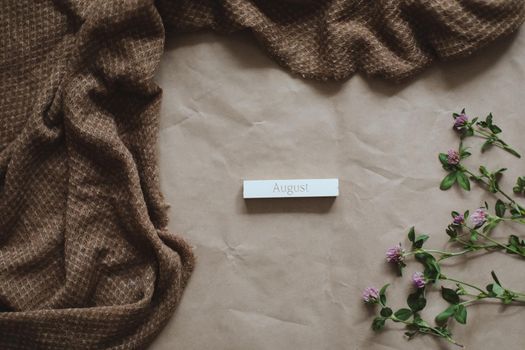 Hello August concept. brown paper texture background with flowers, top view, copyspace.
