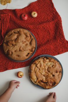 Baby hands reach for the apple cake on white table top view.