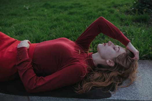 a blonde girl in red lies in the park