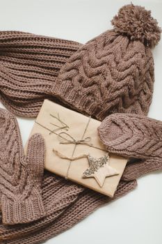 Knitted hat, scarf and mittens and a Christmas gift wrapped in kraft paper on a white table. High quality photo