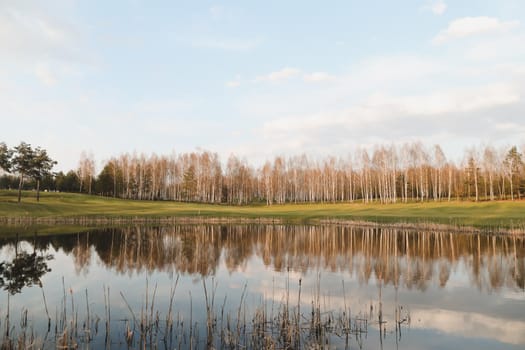 Beautiful colorful summer or spring natural landscape with a lake surrounded by green field and trees in sunlight. Real photo