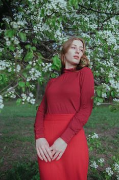 a blonde girl in red unites with nature in a garden of flowering trees