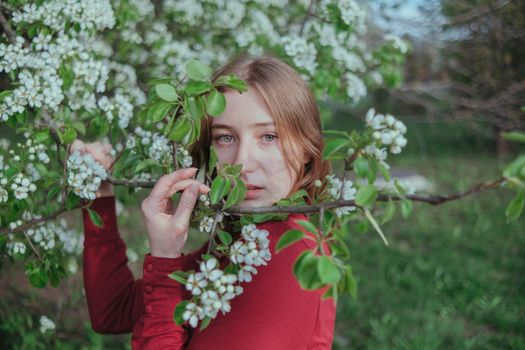 a blonde girl in red hides in flowering trees