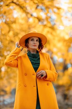 Beautiful woman walks outdoors in autumn. She is wearing a yellow coat, yellow hat and green dress. Young woman enjoying the autumn weather. Autumn content.