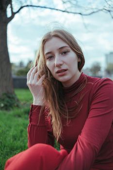 a blonde girl in red sits in the city, her hair is developed by the wind