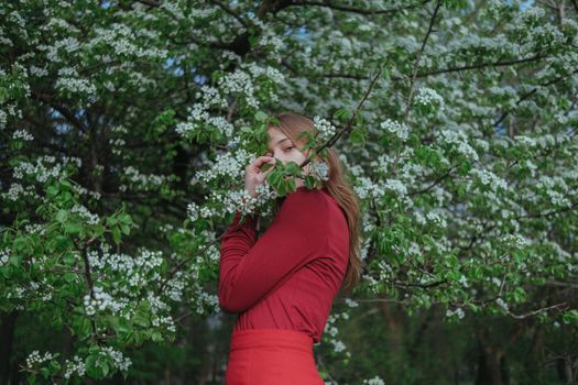 a blonde girl in red hides in flowering trees