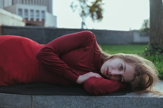 a blonde girl in red lies in the park