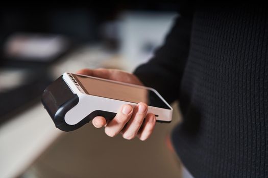 Bank terminal for contactless payment. Acquiring. Young man holds a terminal in his hands.