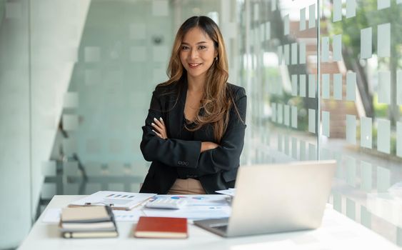 Portrait asian business woman with crossed arms looking at the camera working with laptop computer for accounting financial at office