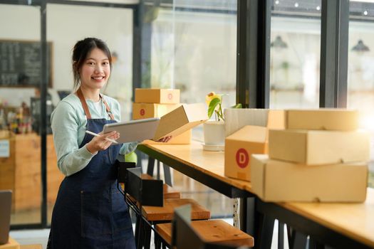 Startup small business SME, Entrepreneur owner using laptop computer taking receive and checking online purchase shopping order to preparing pack product box. Selling online ideas concept.