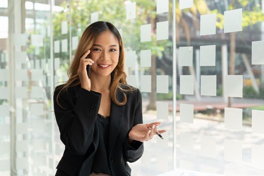 Portrait confident business asian woman calling on mobile phone at office window.
