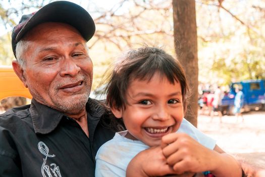 Latino grandfather and his grandson smiling and sitting outside a farm in the countryside of NIcaragua. Concept of family relations of communities in Latin America.