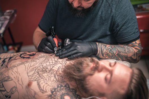 Professional tattoo artist does tattoo on the skin of his client in studio.