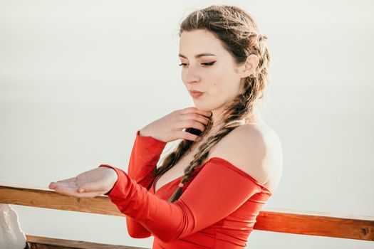 Closeup video portrait of sensual young brunette woman in red dress, happily dancing outdoors isolated on blurry sea background with natural bokeh in soft warm sunset backlight