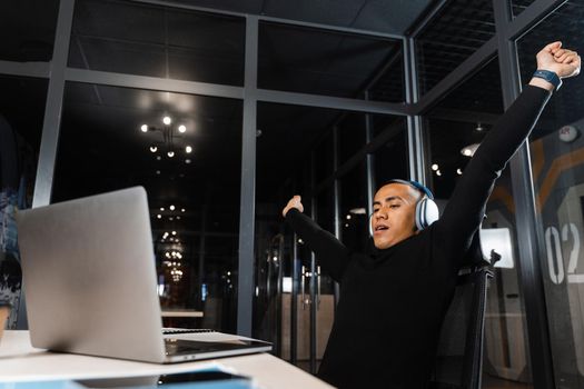 Tired and sleepy Asian man raises his hands up and yawns at the workplace. Work online overtime. Man wants to sleep at work