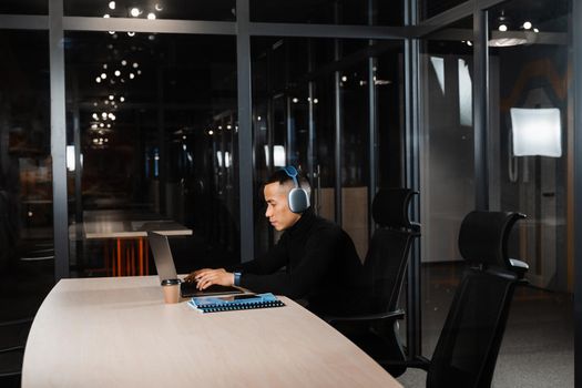 Asian man in headphones working online and listen to music in office. Asian handsome guy with laptop in coworking space