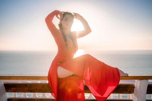 Closeup video portrait of sensual young brunette woman in red dress, happily dancing outdoors isolated on blurry sea background with natural bokeh in soft warm sunset backlight