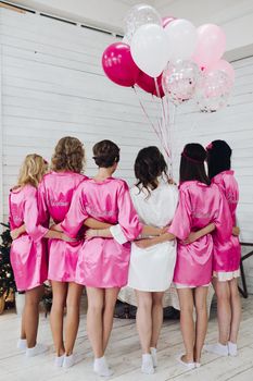 Back view of group of bridesmaids with bride-to-be in beautiful silk robes with different names on their backs.