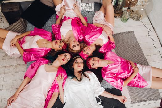 Overhead of attractive young girls in pink robes lying on bed in circle. Bachelorette party.