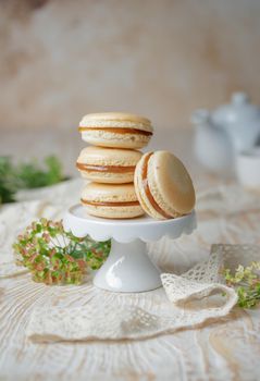 Stack of caramel macaroons on a stand on a wooden background