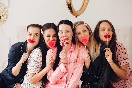 Stock photo portrait of lovely beautiful adult girls smiling at camera holding sweet lollipops in front of their lips. Bachelorette party. Hen party concept. Bridesmaids friends and the bride in the middle with lollipops.