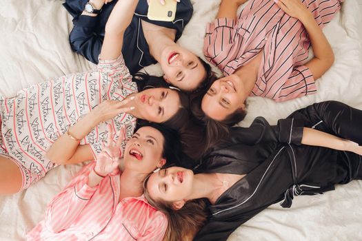 Top view of group of pretty young women in pajamas lying on bed and having fun. Birthday party concept