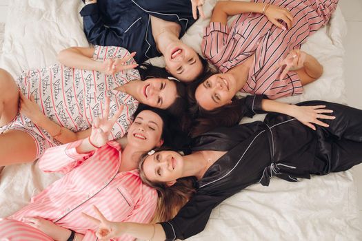 Top view of group of pretty young women in pajamas lying on bed and having fun. Birthday party concept