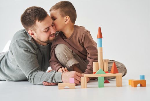 Handsome son kissing his father. Paternity. Dad and his son playing with colored wooden blocks on white background