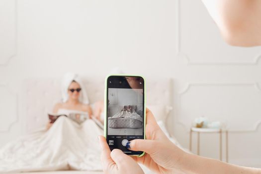 Cropped photo of female hand holding smartphone while making photo of two pretty ladies reading magazine. Care, leisure and relaxation time