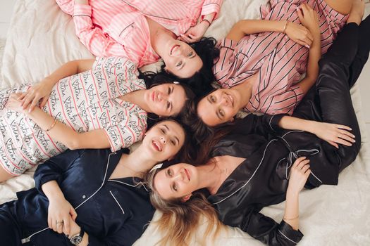 Top view of group of pretty young women in pajamas lying on bed and having fun. Birthday party concept