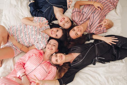 Top view relaxing young girl friends lying on bed having fun posing together medium shot. Group of happy female enjoying pajamas party have positive emotion celebrating holiday