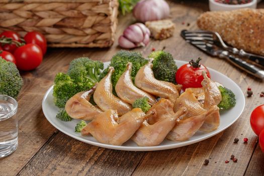Roasted quail wings with vegetables on a wooden table